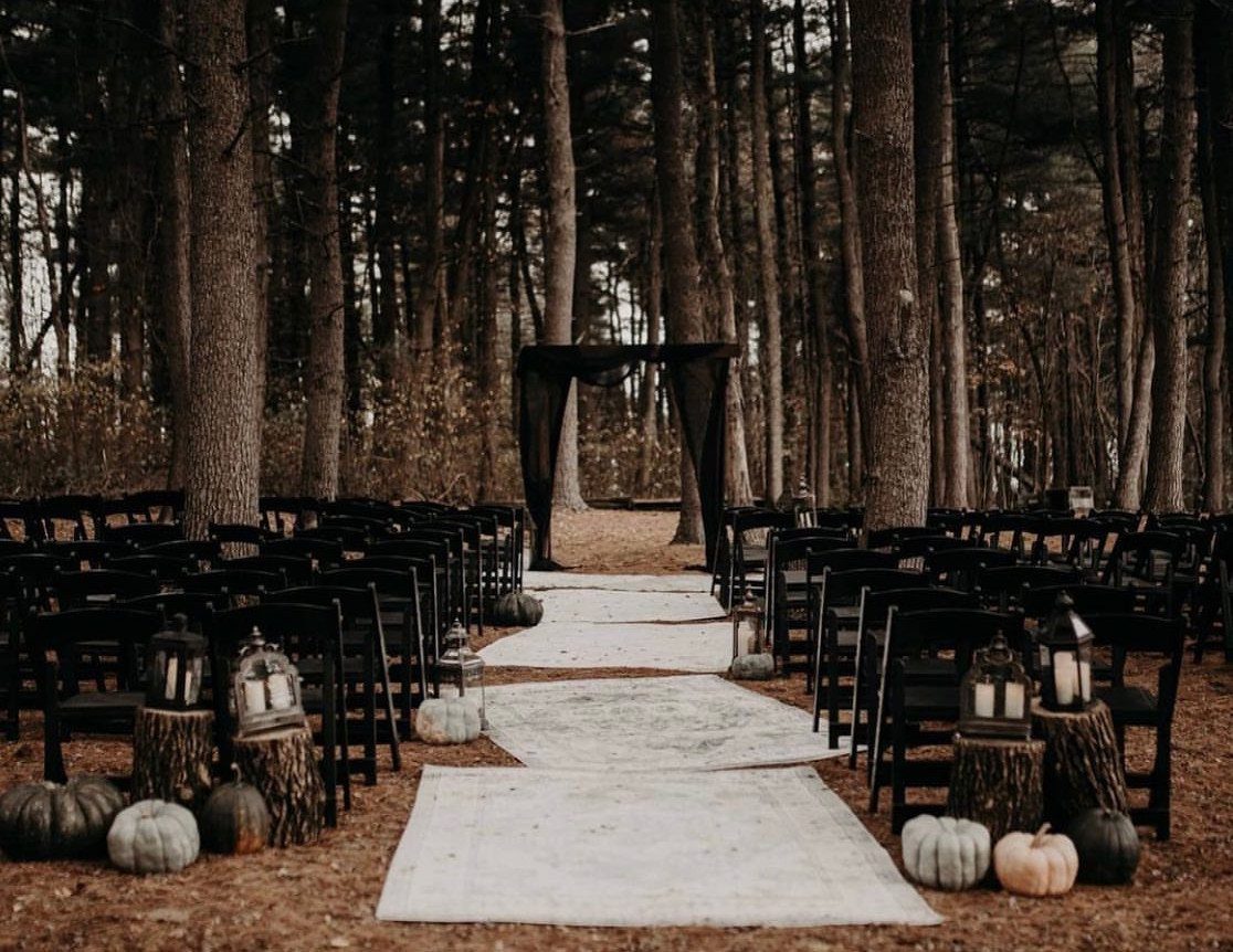 White rug aisle runners laid on the forest floor between rows of black wedding chairs.