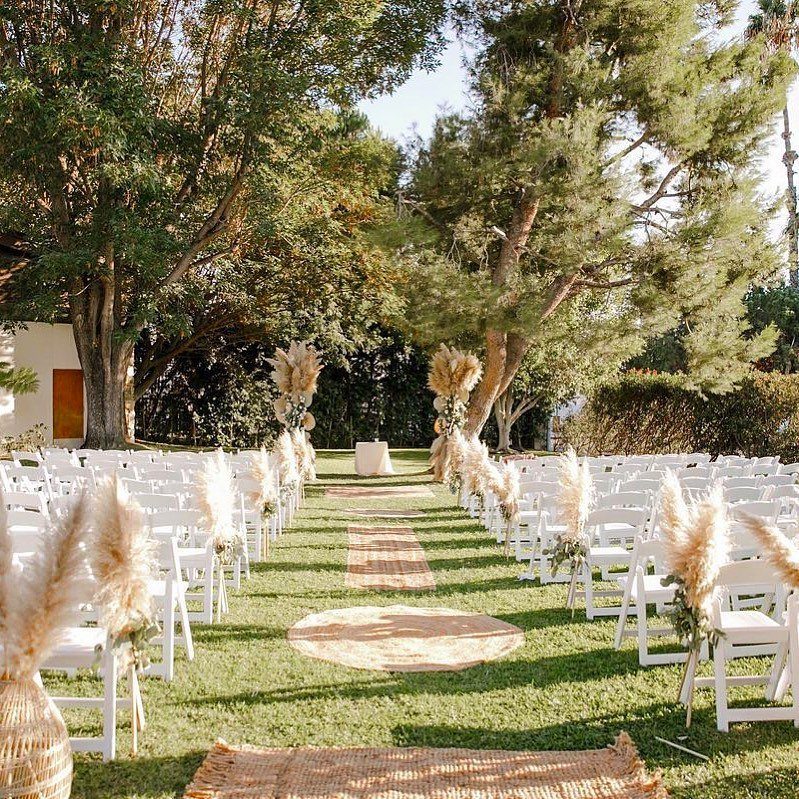 Woven jute rugs forming an aisle between rows of white chairs in a grassy outdoor wedding setting.