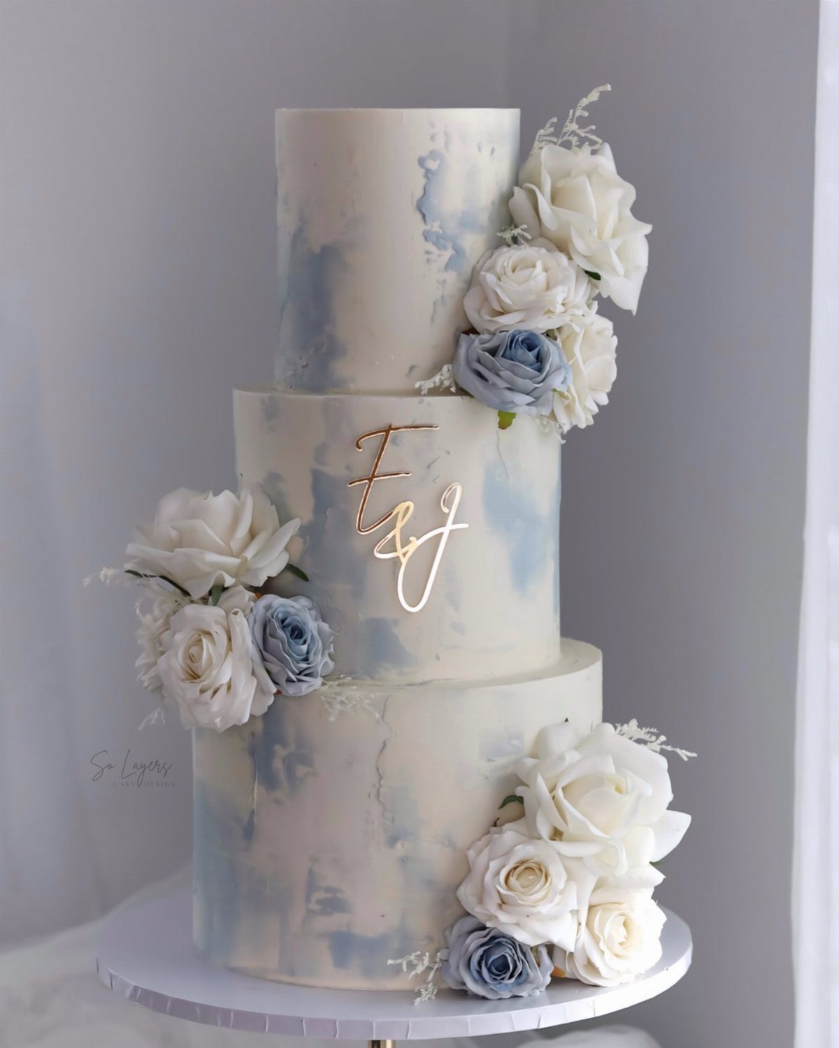 Three-tiered white cake with blue watercolor frosting and white and blue sugar roses.