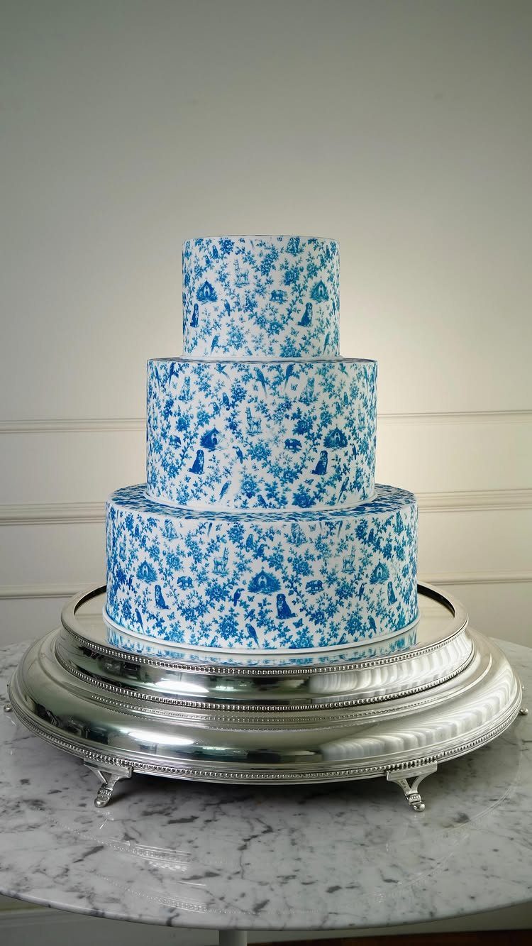 A three-tiered cake with blue and white chinoiserie patterns on a silver stand.
