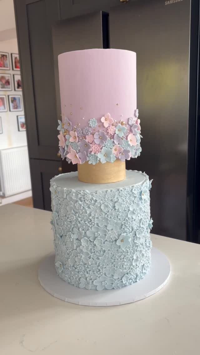 A two-tiered pastel wedding cake with pink and blue floral frosting decorations.