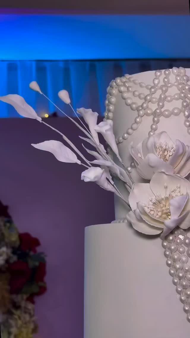 White wedding cake decorated with intricate pearl patterns and large white sugar flowers.