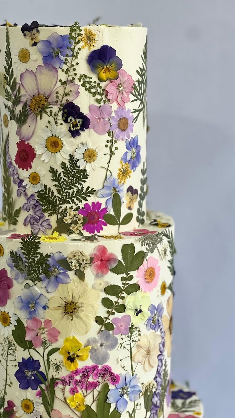 A white tiered cake covered in vibrant pressed wildflowers and green botanical elements.