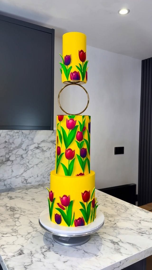 A three-tiered yellow cake decorated with colorful tulip patterns and a gold ring separator.