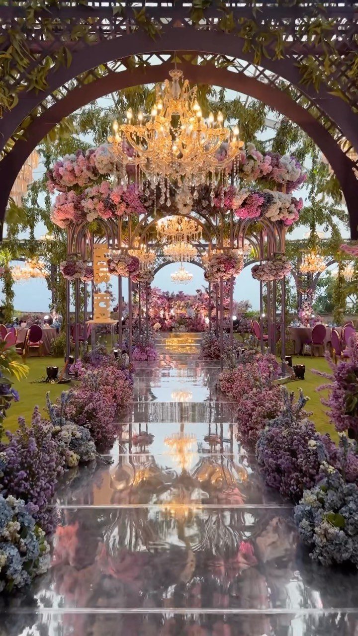 9 Wedding Ceremony Arch Ideas for Indoor and Outdoor Vows 6 Ornate crystal chandeliers hanging from a floral archway over a reflective wedding aisle.