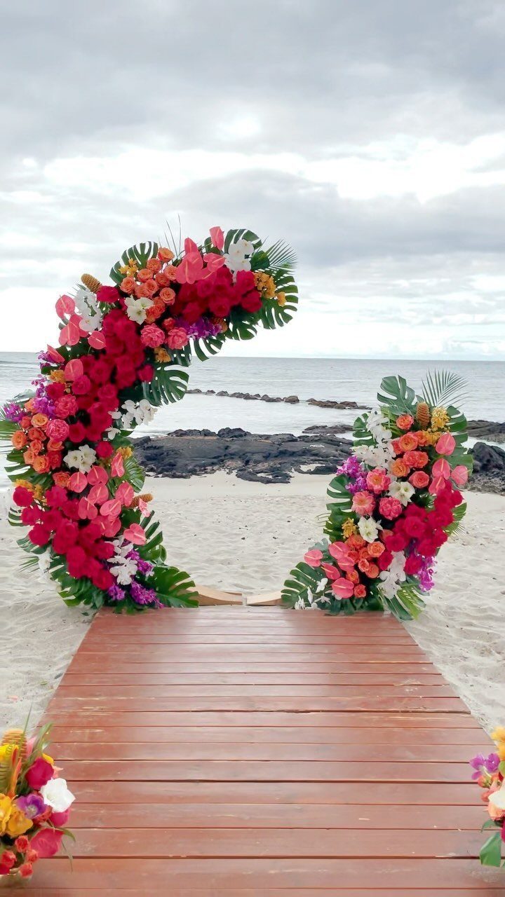 9 Wedding Ceremony Arch Ideas for Indoor and Outdoor Vows 4 A tropical floral wedding arch with pink and orange flowers on a sandy beach.