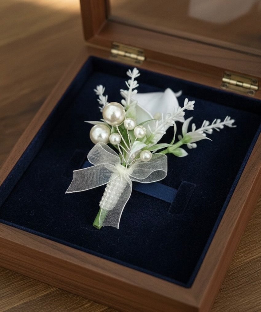 A white calla lily boutonnière with pearls and a sheer ribbon in a wooden box.