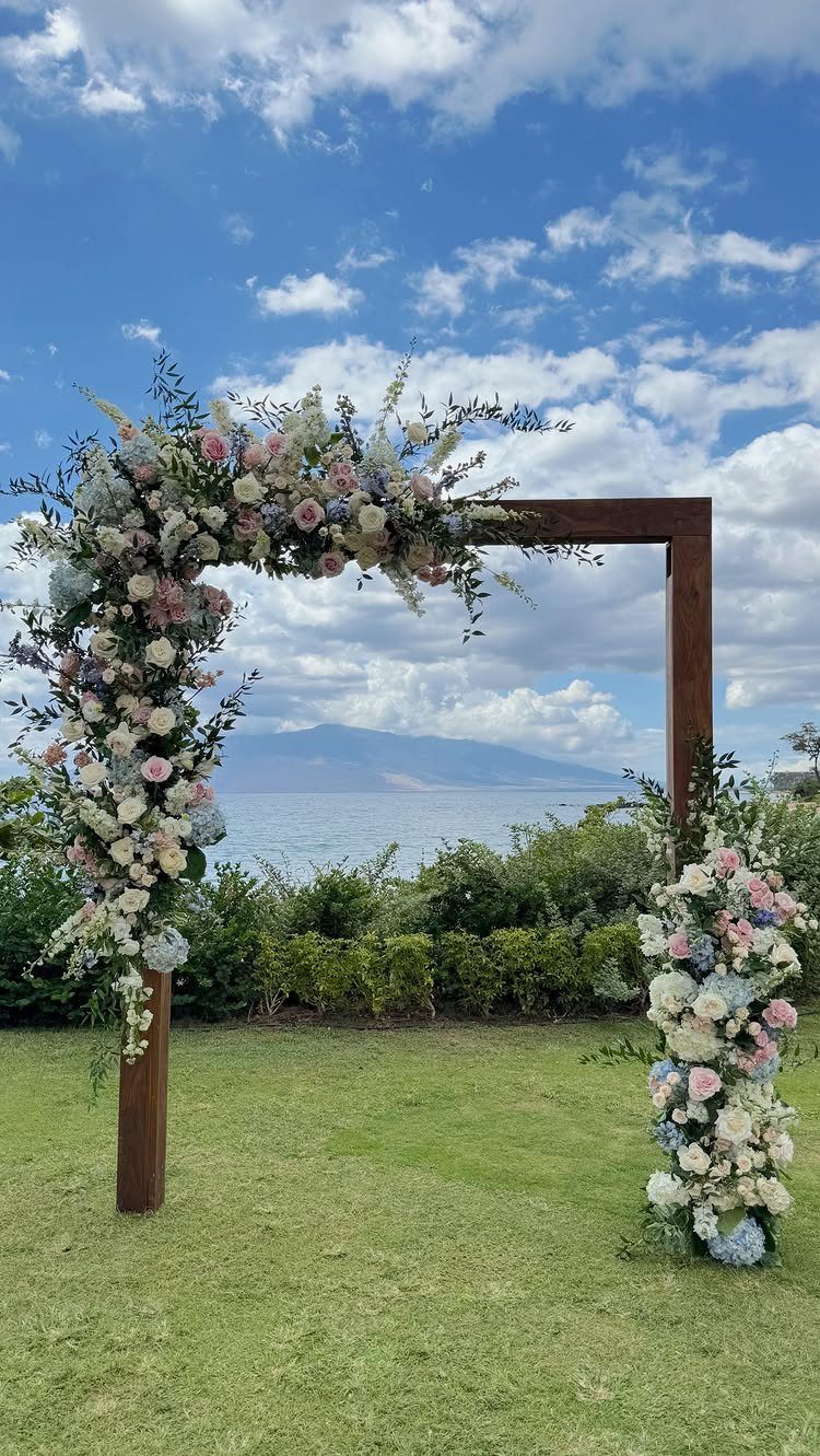 A wooden wedding arch decorated with pink and white flowers overlooking the ocean.