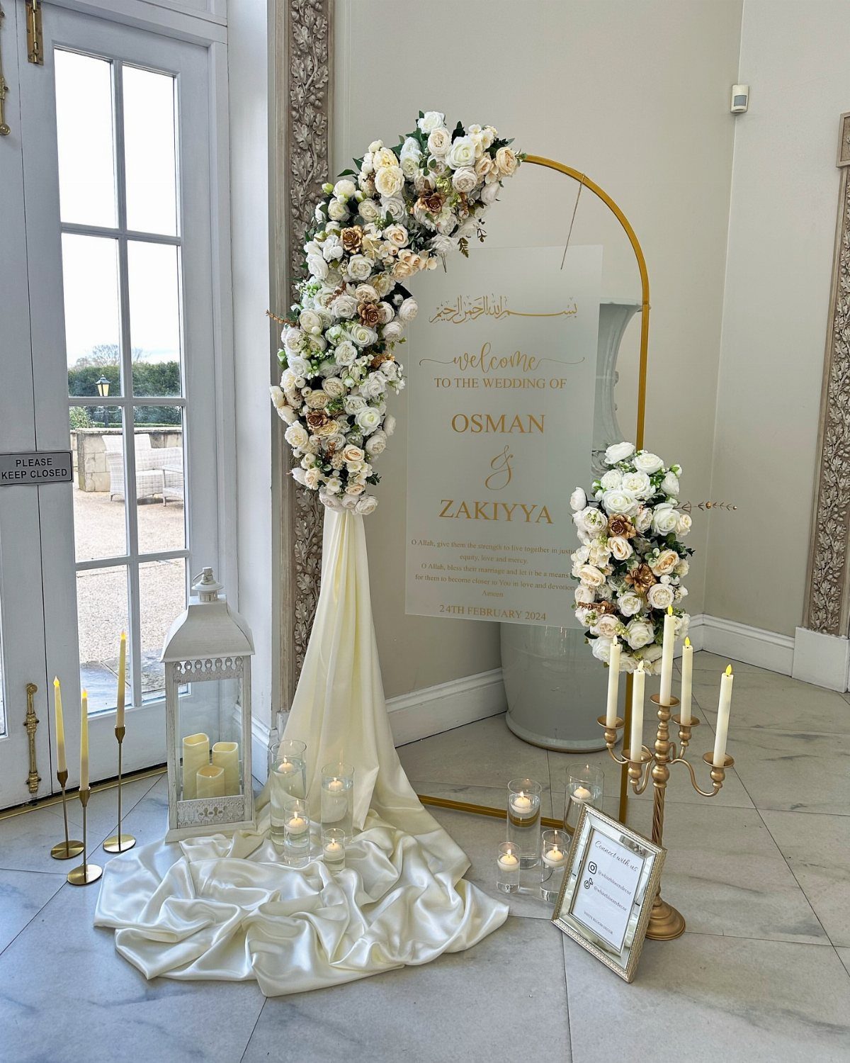 8 Wedding Decor Elegant Ideas for Church and Reception (2026) 8 A gold circular wedding welcome sign decorated with white flowers and draped cream fabric on a marble floor.