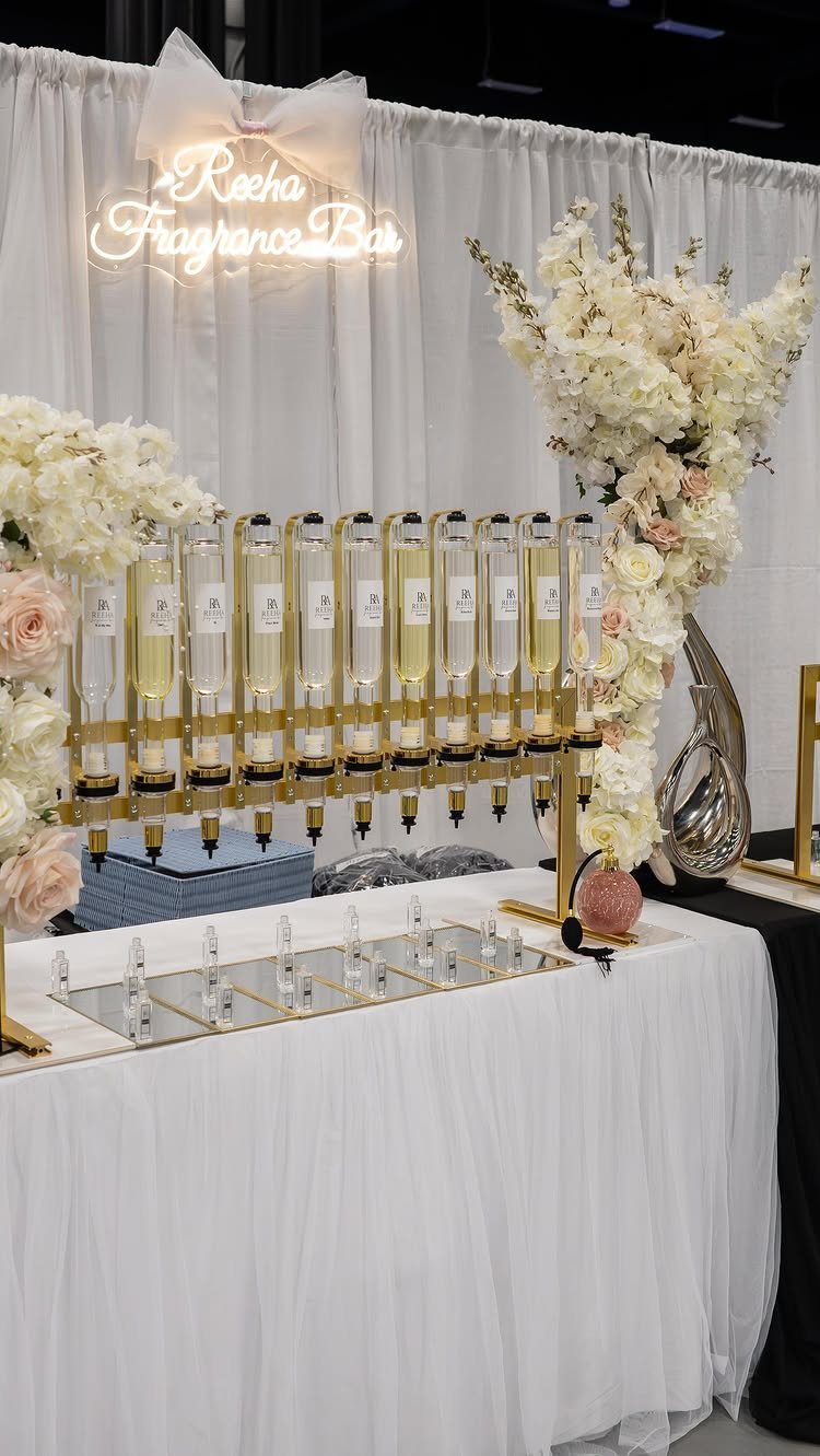 12 Wedding Events Ideas for Your Reception, Ceremony & More 1 A white fragrance bar display with glass perfume bottles and large white floral arrangements.