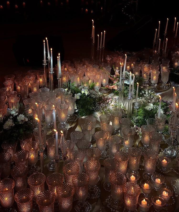 12 Wedding Events Ideas for Your Reception, Ceremony & More 10 Many glowing candles and glass votives arranged with greenery on a dark wedding table.