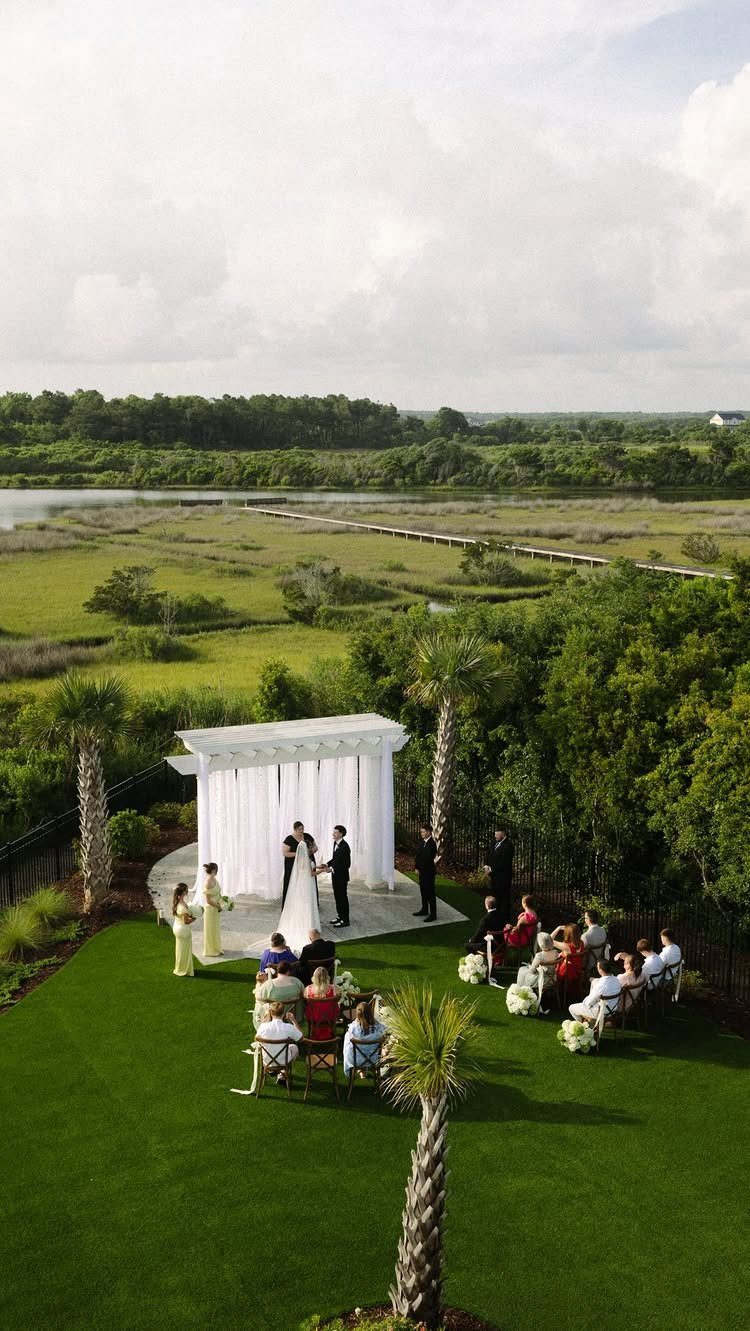 12 Wedding Events Ideas for Your Reception, Ceremony & More 8 A small wedding ceremony held on a green lawn overlooking a scenic marshland landscape.