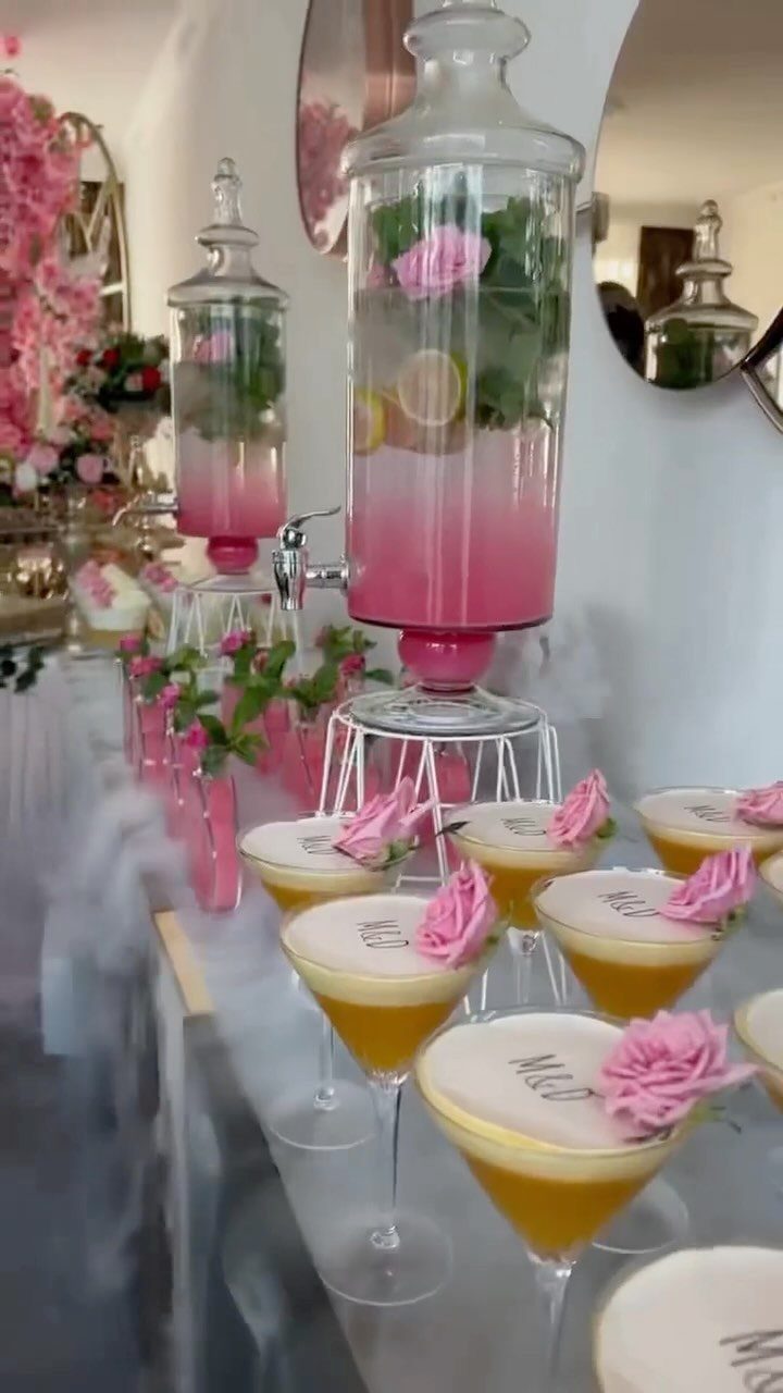 12 Wedding Events Ideas for Your Reception, Ceremony & More 3 Pink drinks in glass dispensers and yellow rose-garnished cocktails on a table with white smoke.