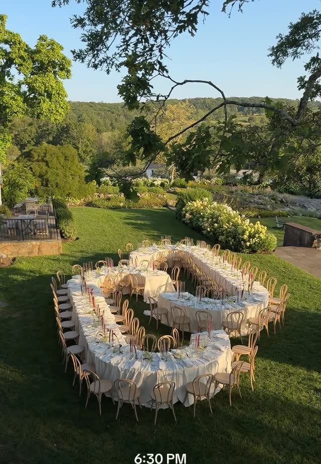 12 Wedding Events Ideas for Your Reception, Ceremony & More 5 A large U-shaped dining table set with cream linens and wooden chairs on a grassy lawn.