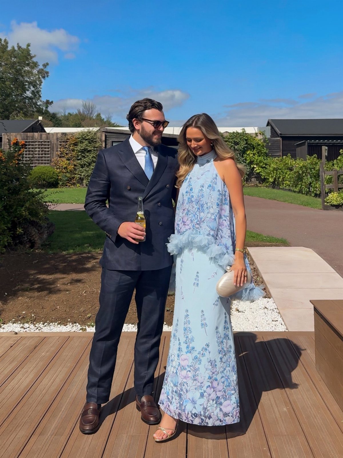 A man in a navy suit and a woman in a blue floral maxi dress standing outdoors.