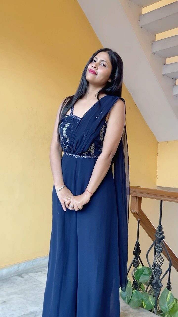 Woman in a navy blue sequined jumpsuit posing against a yellow wall near a staircase.