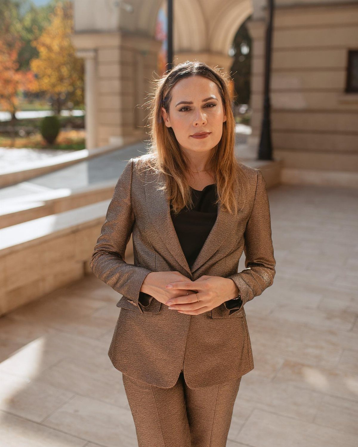 Woman in a shimmering gold metallic pantsuit standing outdoors in front of a stone building.