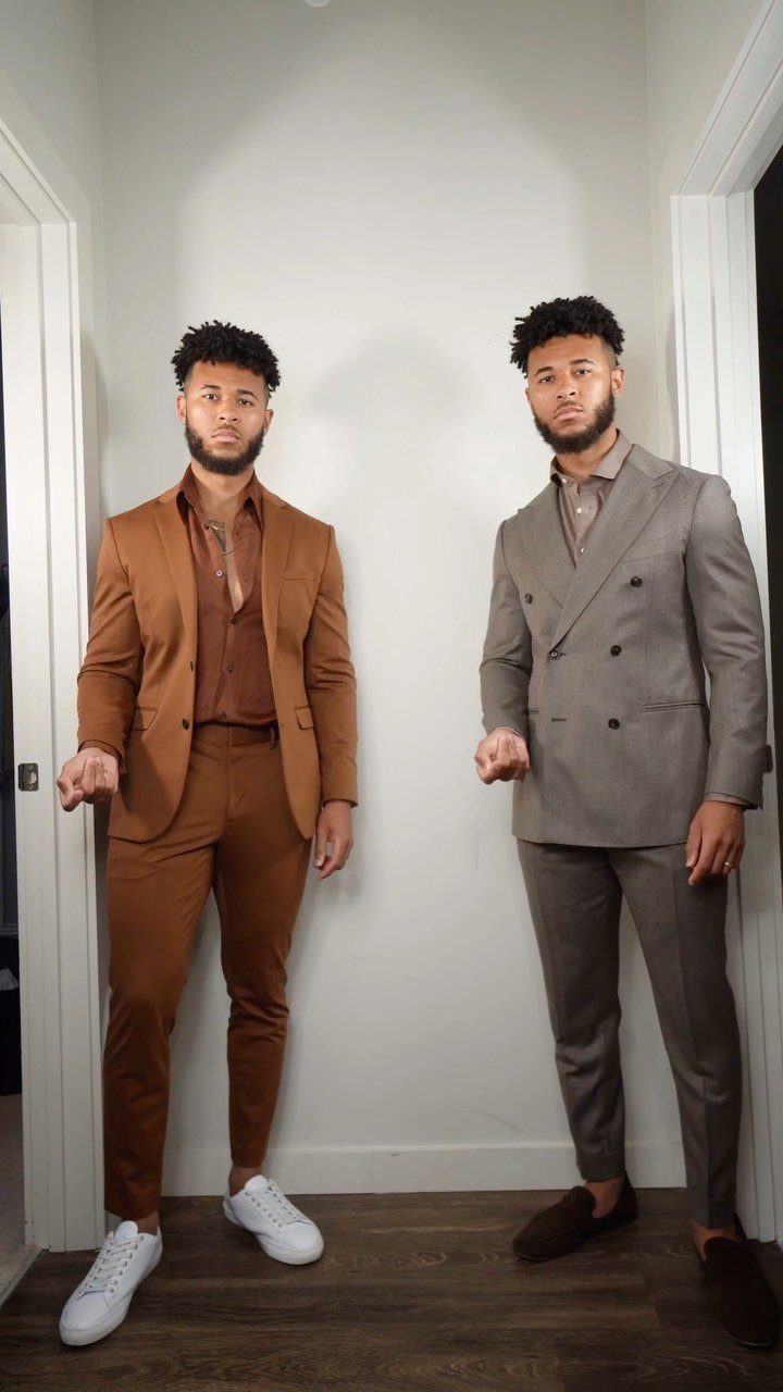 Two men posing in stylish brown and grey suits against a white wall.