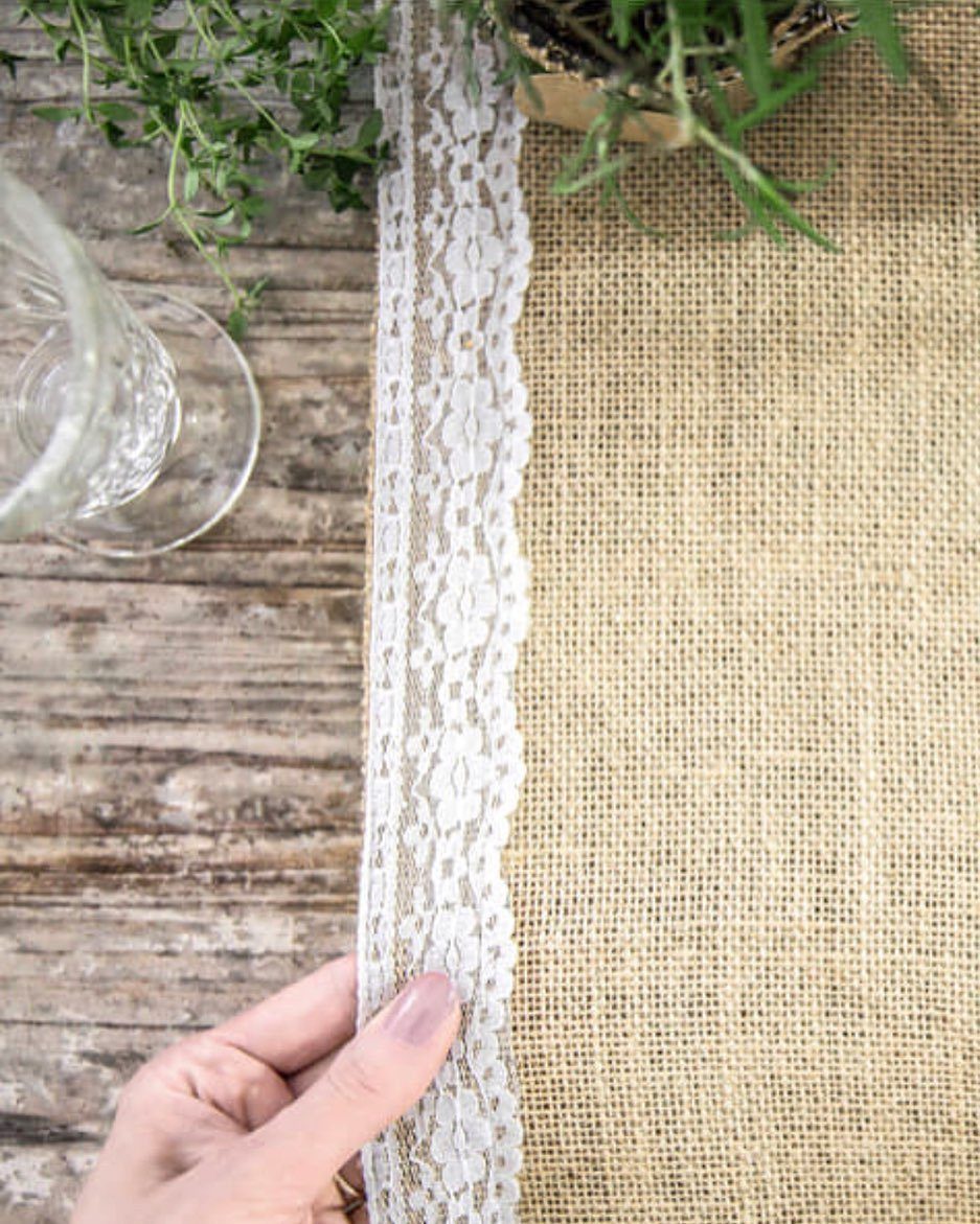 13 Wedding Ideas for Country Ceremonies That Feel Lived-In 13 A hand holding a burlap table runner decorated with white lace on a wooden table.