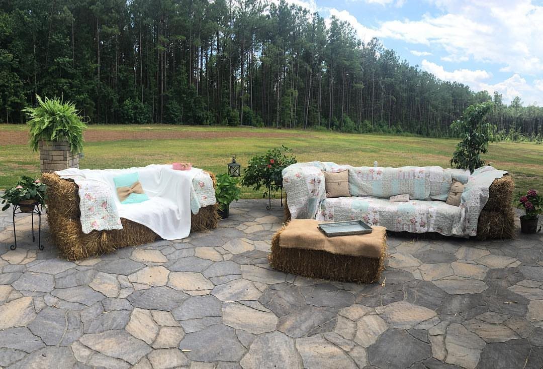 13 Wedding Ideas for Country Ceremonies That Feel Lived-In 7 Hay bale sofas with floral fabric cushions arranged on a stone patio near a forest.