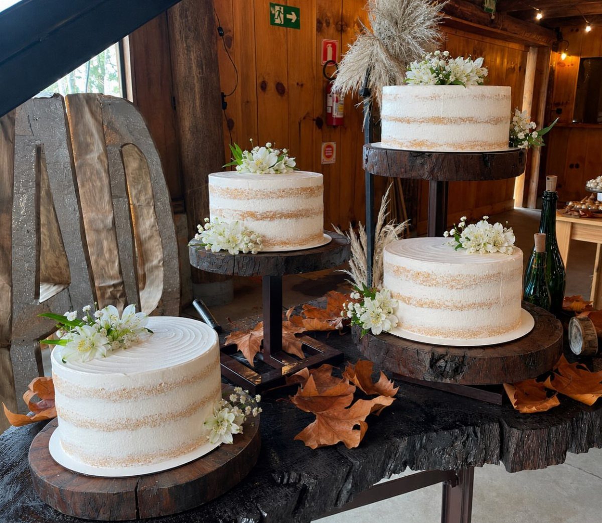 13 Wedding Ideas for Country Ceremonies That Feel Lived-In 3 Three white naked cakes with small white flowers on rustic wooden stands atop a wooden table.