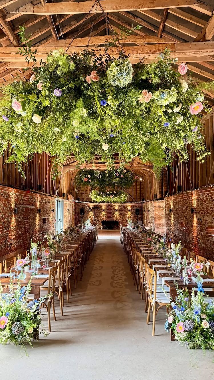 13 Wedding Ideas for Country Ceremonies That Feel Lived-In 2 Long dining tables set with flowers inside a rustic brick barn with hanging floral arrangements.
