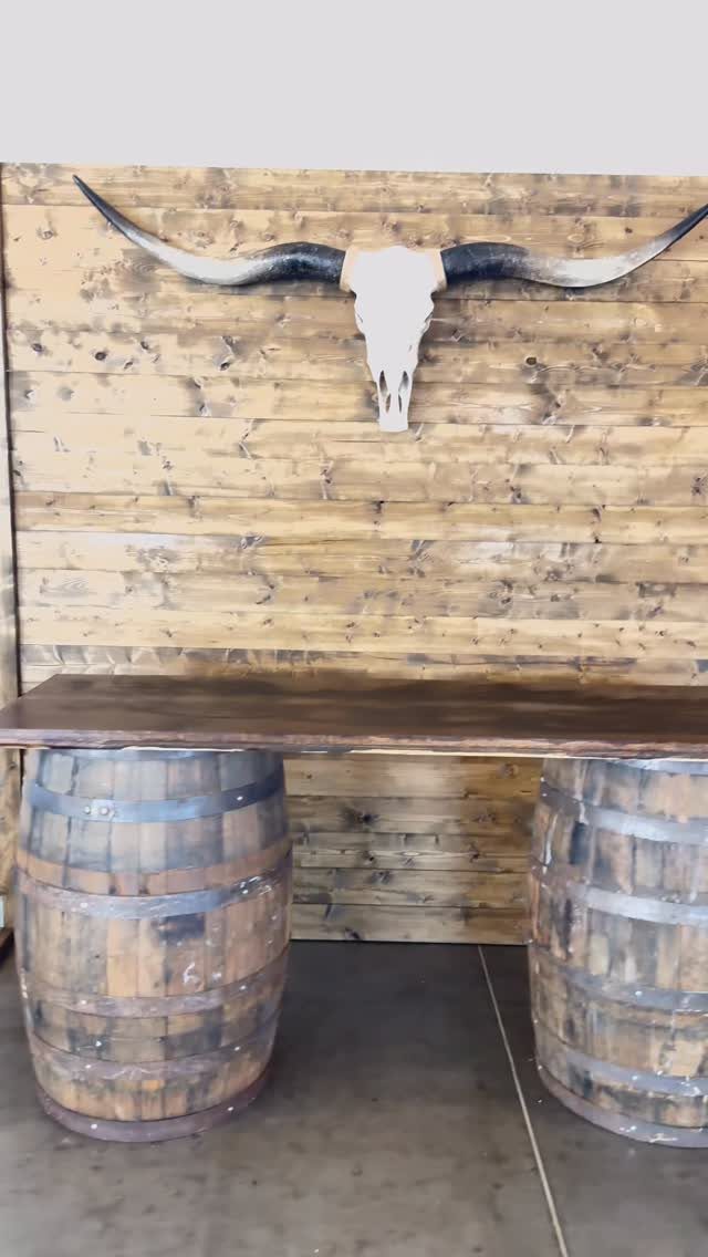 13 Wedding Ideas for Country Ceremonies That Feel Lived-In 6 Two wooden wine barrels supporting a long tabletop against a wood plank wall with a longhorn skull.