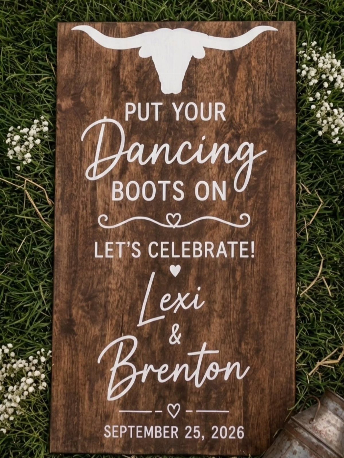 13 Wedding Ideas for Country Ceremonies That Feel Lived-In 12 Wooden wedding sign with longhorn skull and white lettering resting on green grass and flowers.