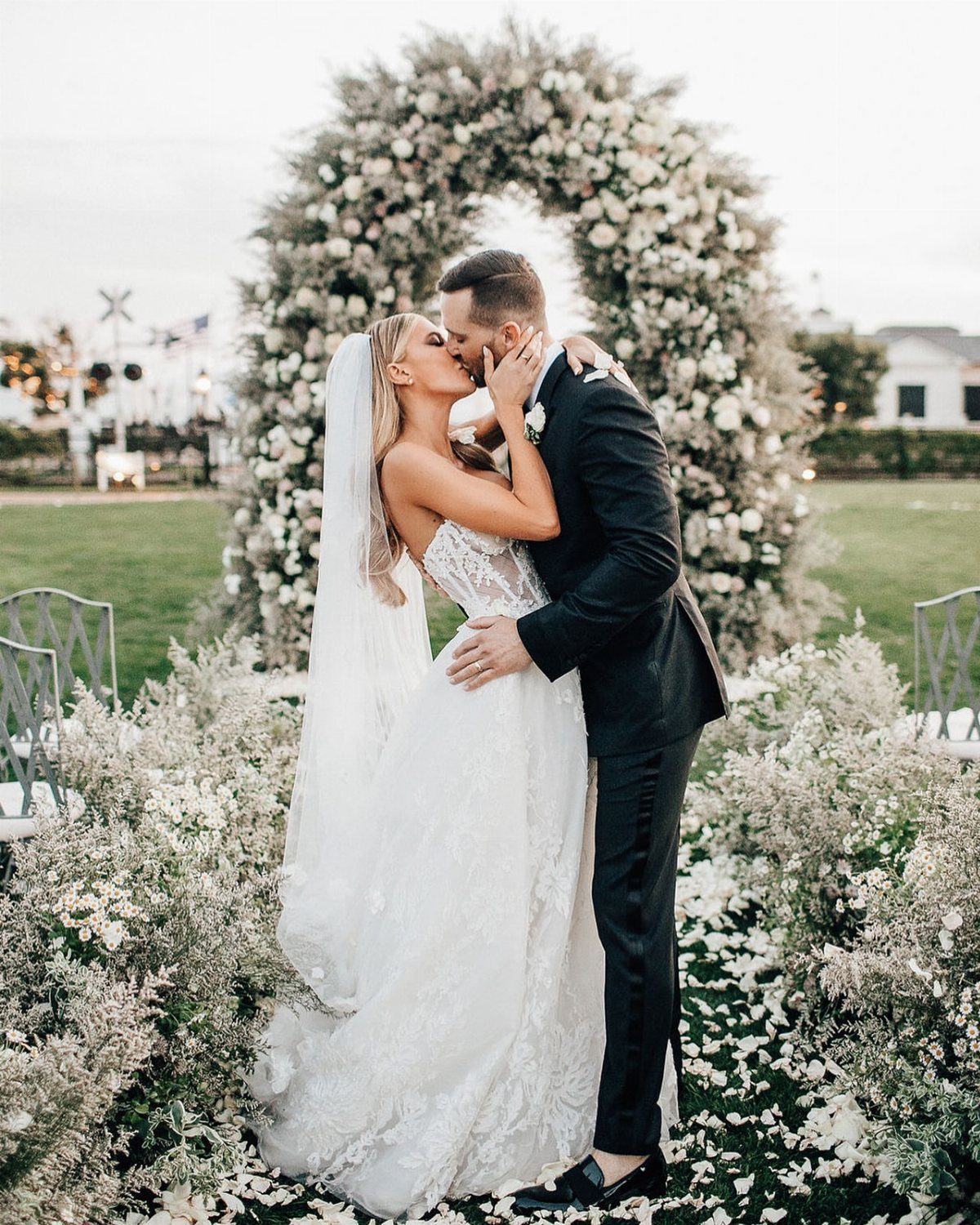 7 Wedding Picture Poses for the First Look, Sunset, and More 3 A bride and groom kissing in front of a large white floral wedding arch.