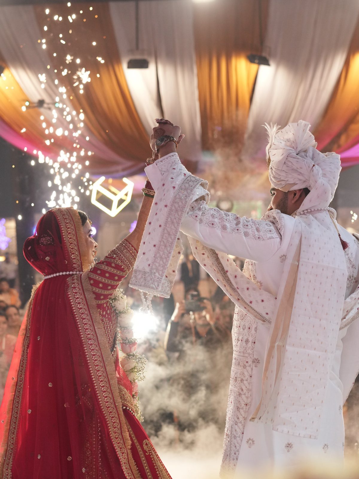 7 Wedding Picture Poses for the First Look, Sunset, and More 2 A bride in red and a groom in white dance together amidst smoke and sparkles.