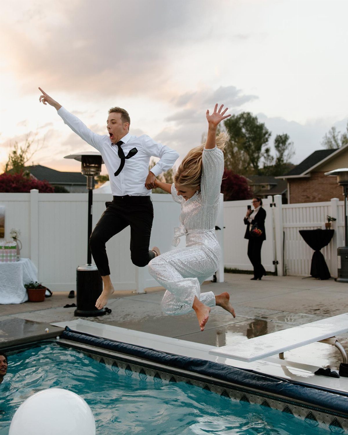 7 Wedding Picture Poses for the First Look, Sunset, and More 4 A man and woman in formal attire jumping into a swimming pool mid-air.