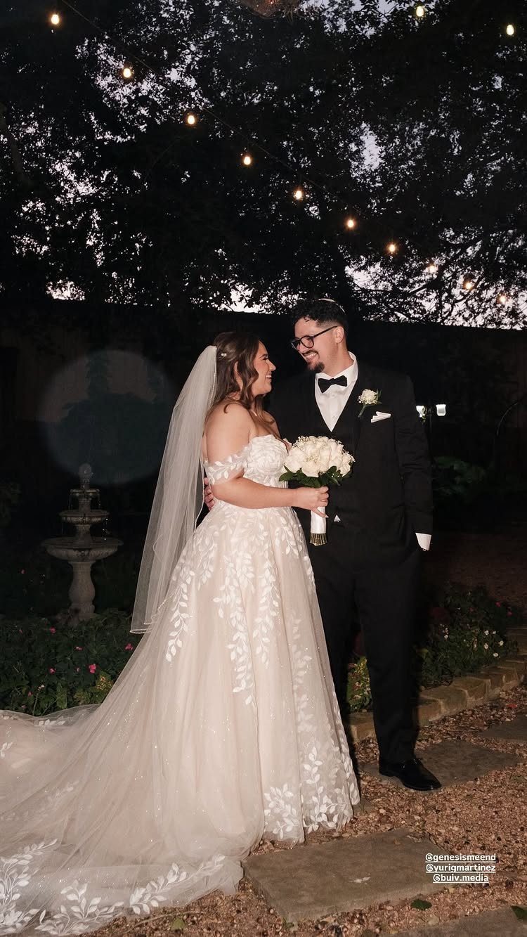 7 Wedding Picture Poses for the First Look, Sunset, and More 6 Bride and groom smiling at each other while standing outdoors under hanging string lights at night.