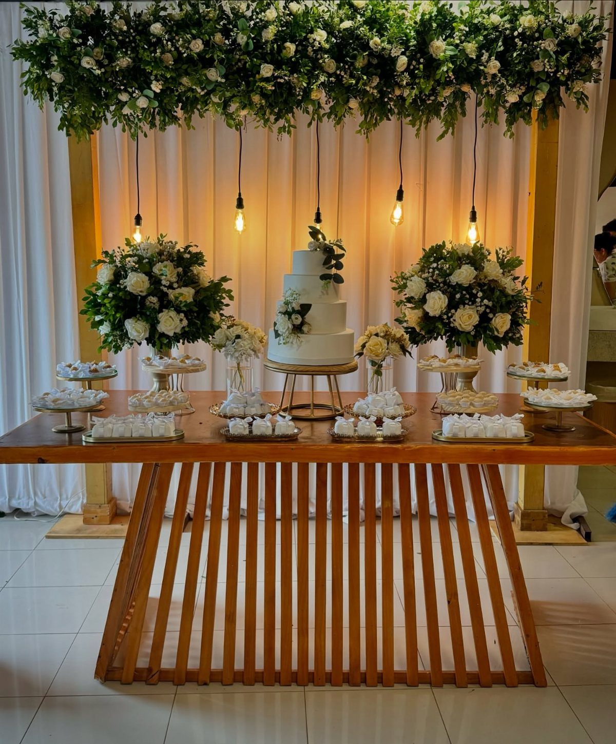 16 Wedding Reception Tables and Layouts for Every Celebration 7 A white wedding cake sits on a wooden table decorated with white flowers and greenery.