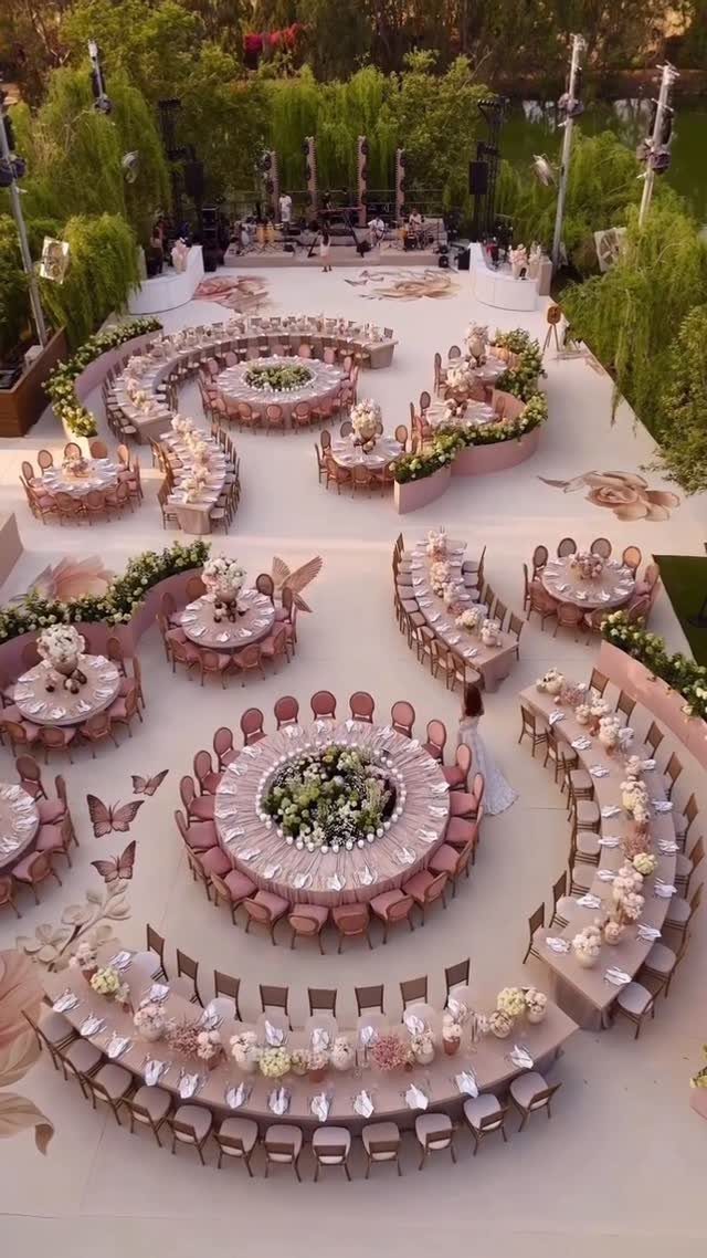 16 Wedding Reception Tables and Layouts for Every Celebration 13 Circular and curved wedding reception tables with pink linens and white floral arrangements in an outdoor setting.