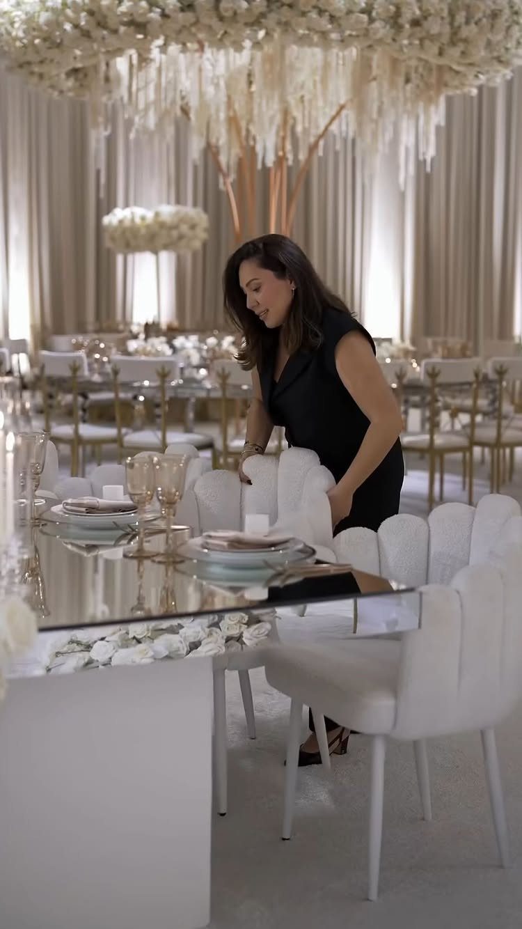 16 Wedding Reception Tables and Layouts for Every Celebration 16 A woman setting a white chair at a mirrored wedding reception table with floral decorations.