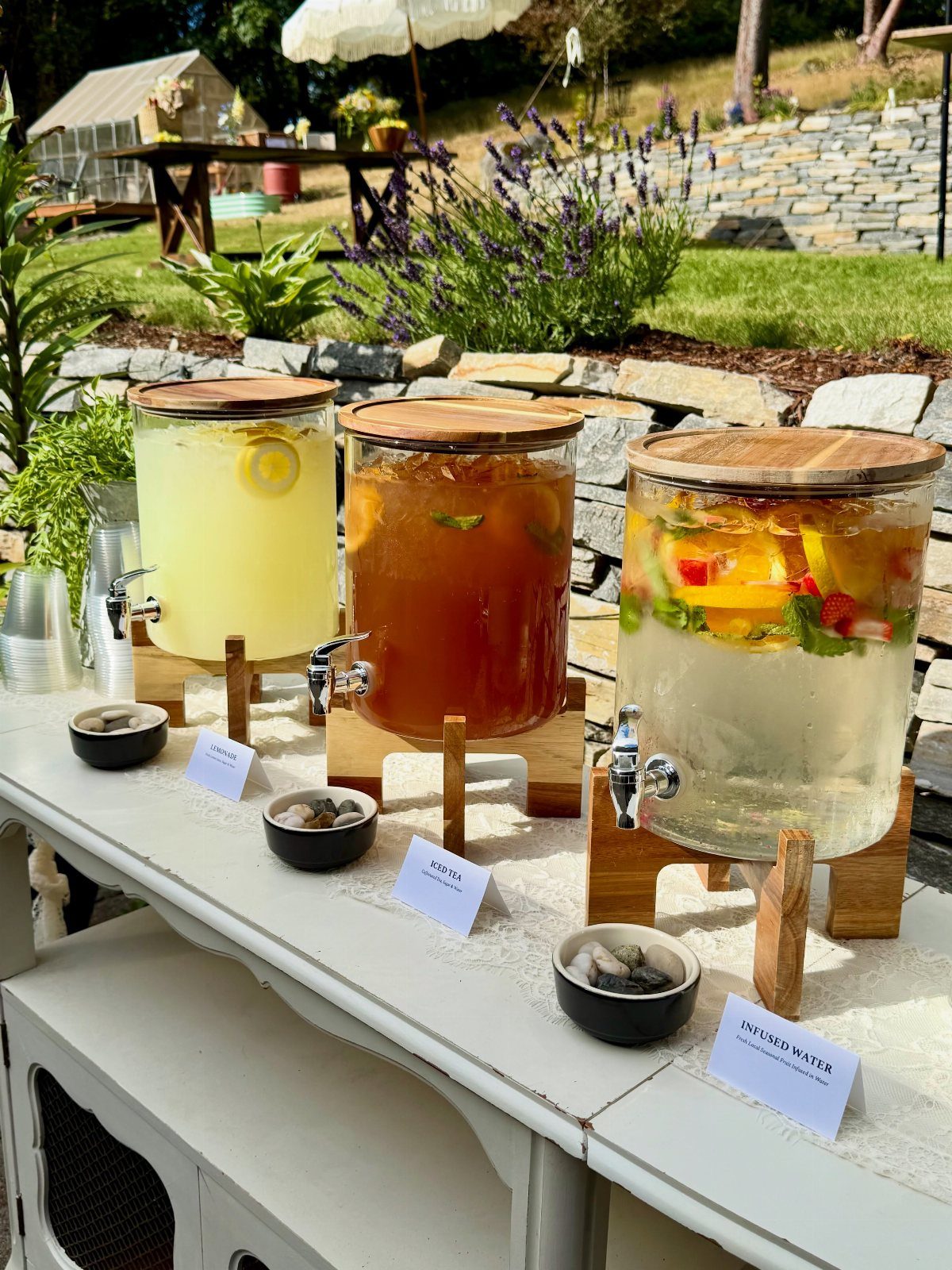 16 Wedding Reception Tables and Layouts for Every Celebration 10 Three glass beverage dispensers filled with lemonade, iced tea, and fruit water on a white table.