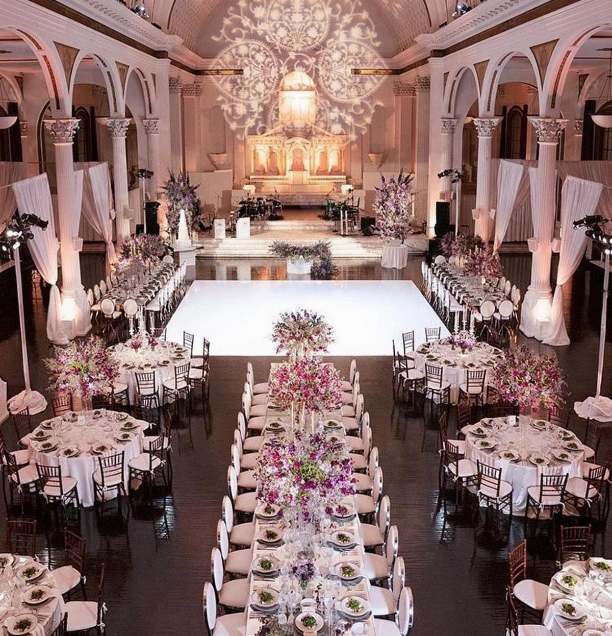 16 Wedding Reception Tables and Layouts for Every Celebration 2 Elegant wedding reception hall with decorated round and rectangular tables and a white dance floor.