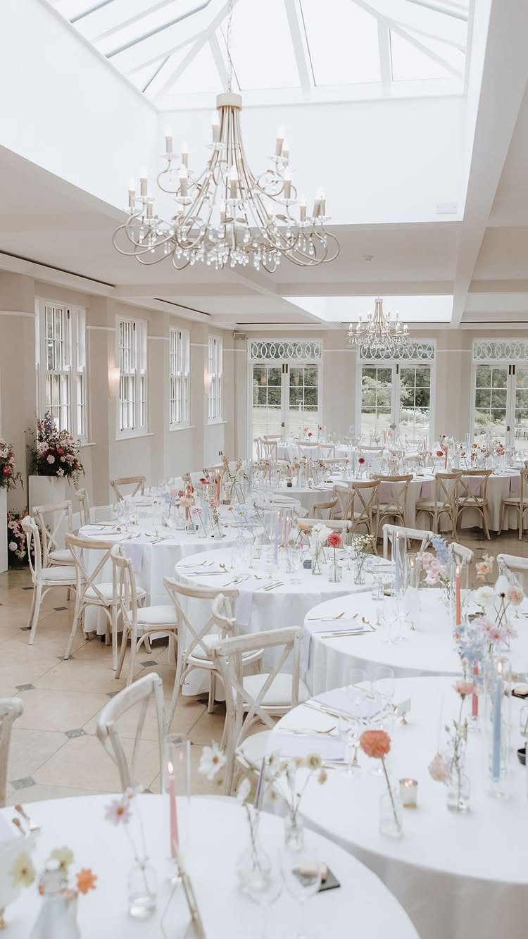 16 Wedding Reception Tables and Layouts for Every Celebration 1 Round wedding reception tables with white linens and floral centerpieces in a bright ballroom.