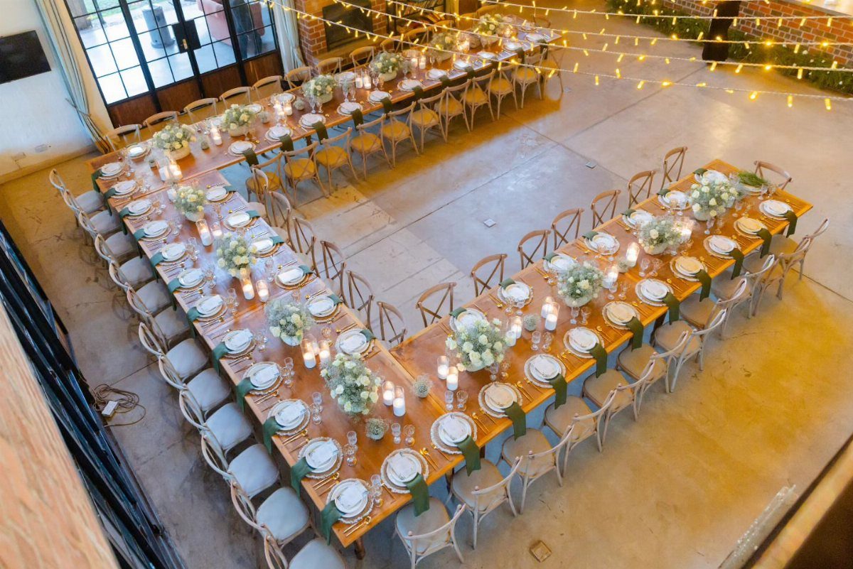 16 Wedding Reception Tables and Layouts for Every Celebration 4 A large U-shaped wedding reception table arrangement with white flowers and greenery in an industrial space.