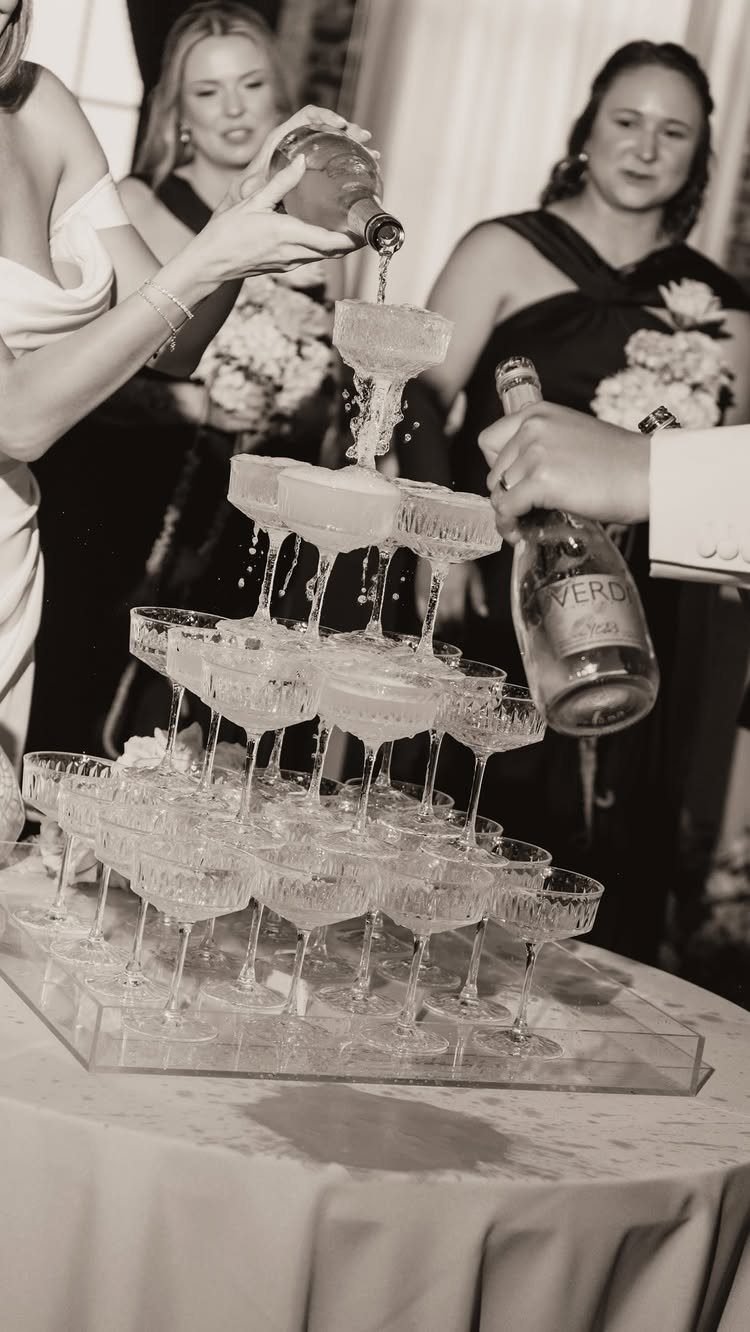 Champagne being poured into a tiered pyramid of coupe glasses at a formal event.