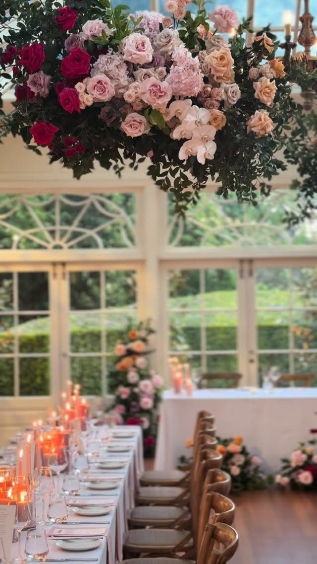 Large pink and red rose floral installation hanging above a decorated wedding reception table.