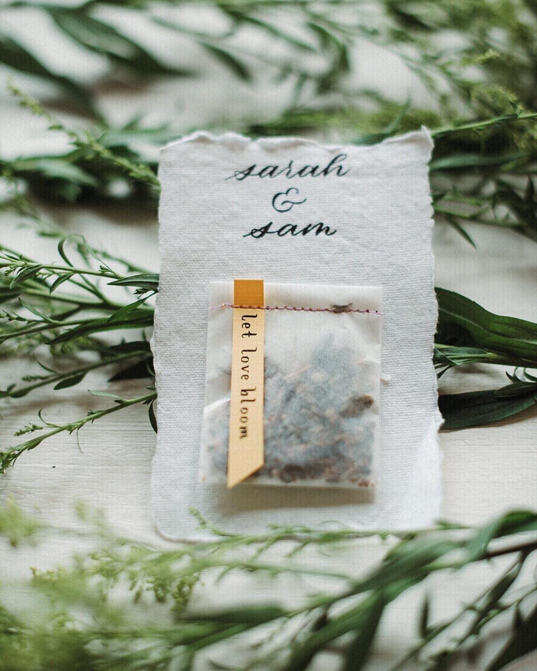 Wildflower Wedding Theme: 13 Ideas for a Light, Natural Day 6 Seed packet with a yellow ribbon and handwritten names resting on green leafy branches.