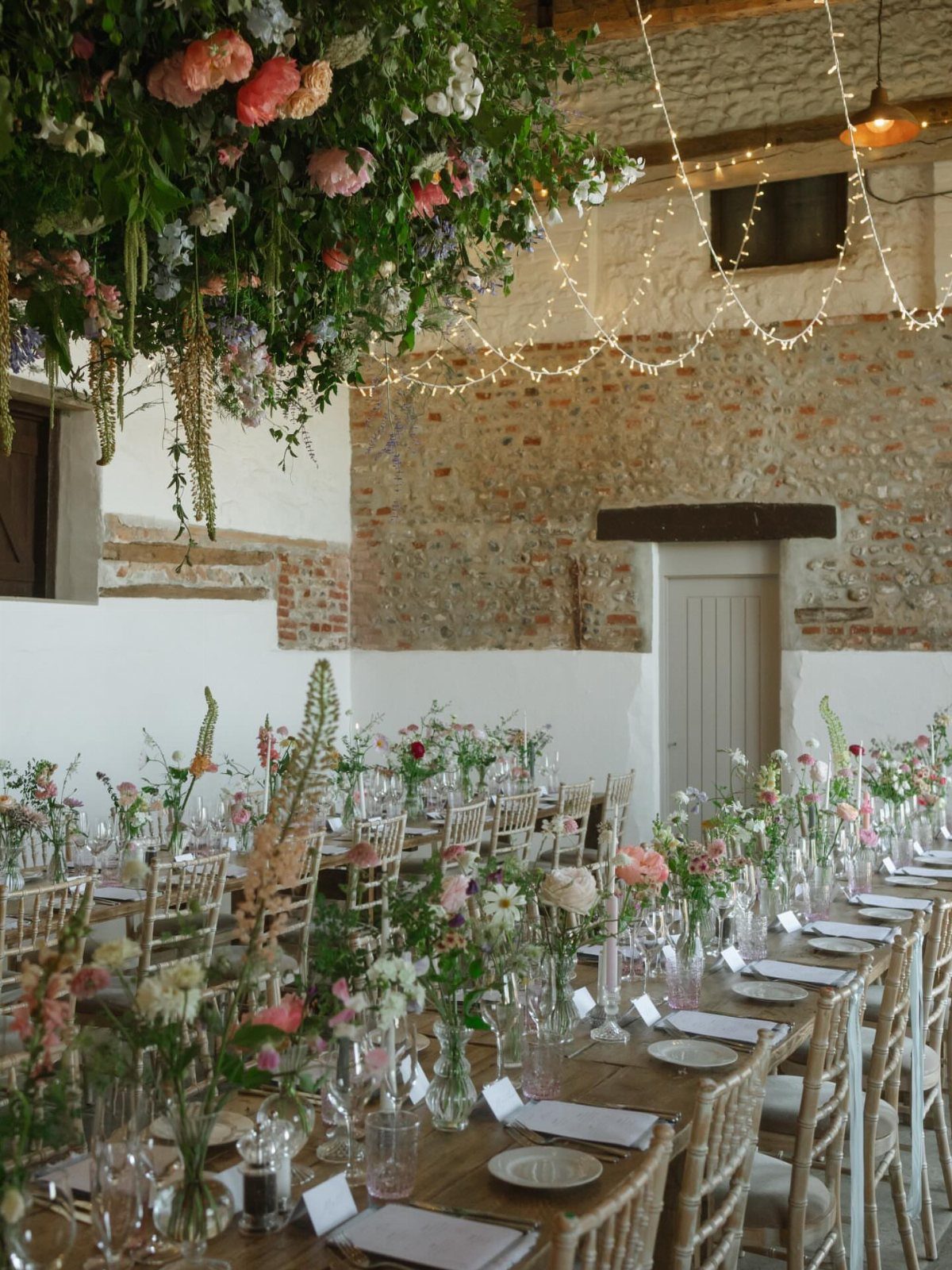 Wildflower Wedding Theme: 13 Ideas for a Light, Natural Day 5 Long wooden dining tables decorated with wildflower arrangements and fairy lights in a rustic stone building.