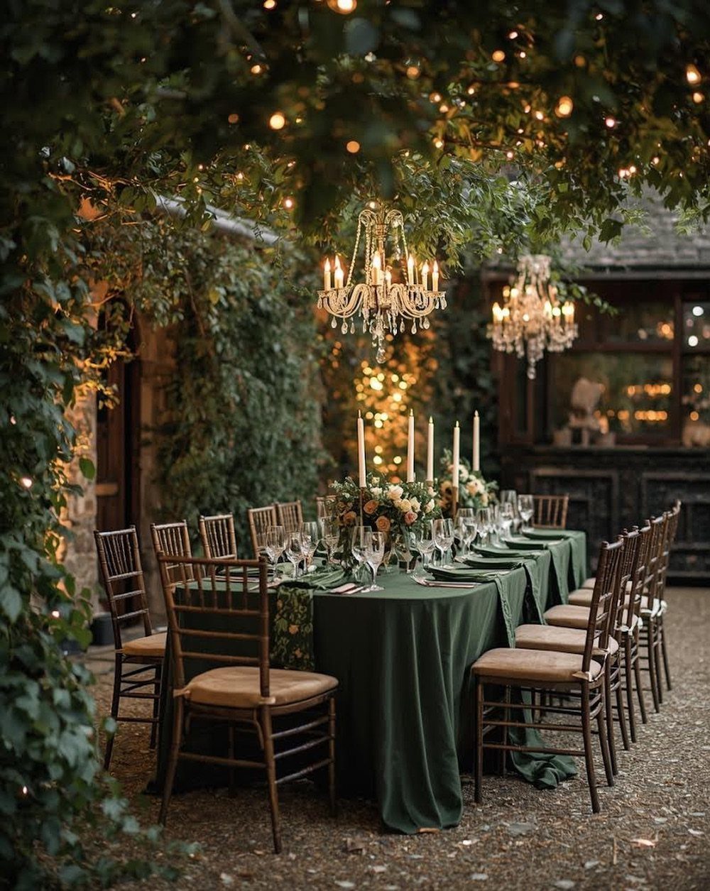 A long outdoor wedding table set with dark green linens, white candles, and sparkling lights.