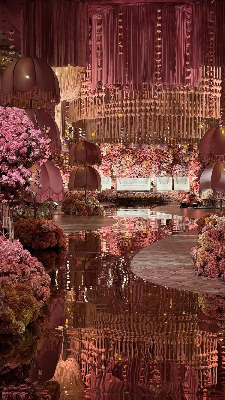 Pink floral arrangements and hanging fabric decorations reflected in a glossy floor at a formal event.