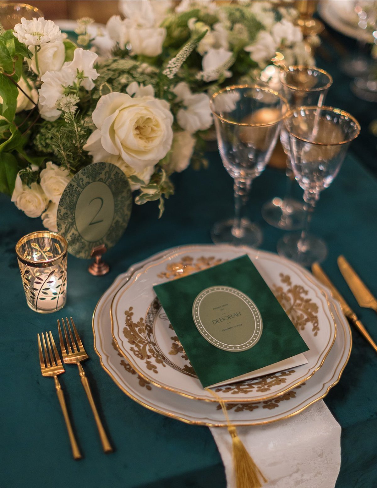 Elegant wedding table setting with white roses, gold cutlery, and emerald green accents.