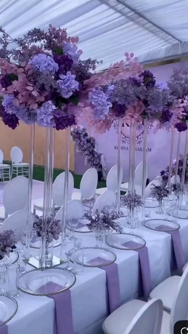 Lavender and purple floral arrangements in tall glass vases on a wedding reception table.