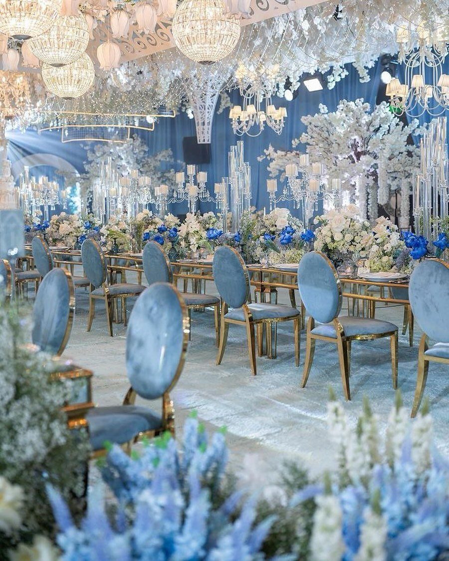 Blue velvet chairs and white floral arrangements decorate a wedding reception with crystal chandeliers.