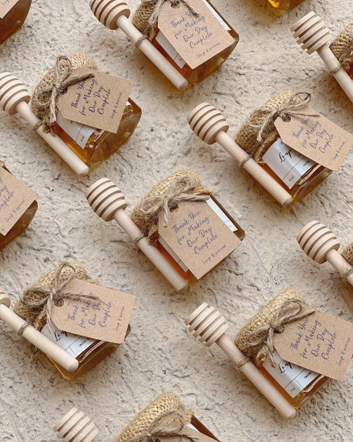 Small honey jars with burlap lids, wooden dippers, and personalized thank you tags on a neutral surface.